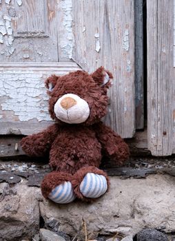 little teddy bear sits on the doorstep near an old door with cracked paint, close up