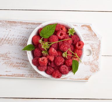 ripe red raspberries in a white wooden plate on a table of boards, textile towel, top view