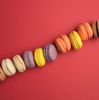 round multi-colored baked macarons with cream lie in a line on a red background, flat lay, copy space 