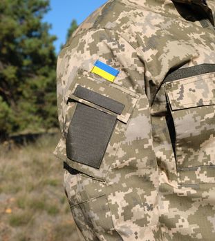 fragment of the hand of a Ukrainian soldier in military camouflage uniform with a patch of the Ukrainian flag, close up