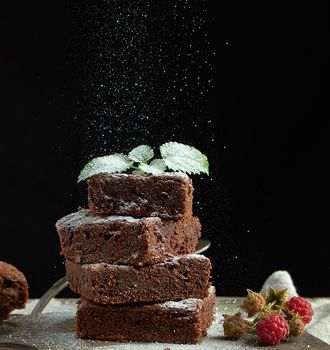 stack of square baked brownie chocolate cake slices sprinkled with white sugar, small particles fly down, low key