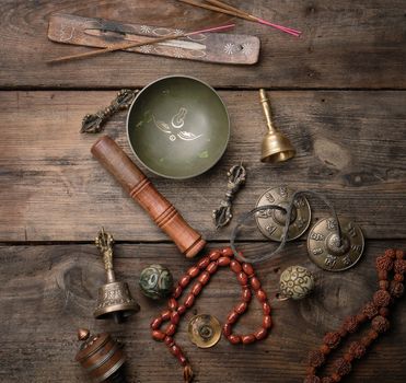 Copper singing bowl, prayer beads, prayer drum and other Tibetan religious objects for meditation and alternative medicine on a brown wooden background