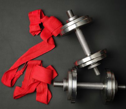 pair of shiny steel typesetting dumbbells for bodybuilding and textile bandage on a black background, top view