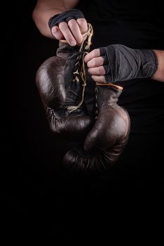 sportsman in black uniform holds old vintage leather boxing gloves, low key