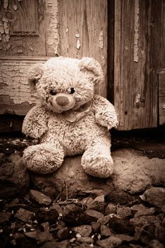 little teddy bear sits on the doorstep near an old door with cracked paint, concept of depression and nostalgia