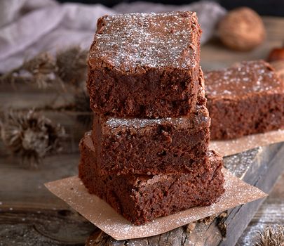 stack of baked square pieces of brownie pie on a wooden board, close up