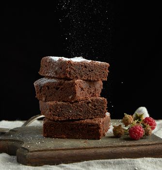 stack of square baked brownie chocolate cake slices sprinkled with white sugar, small particles fly down, low key