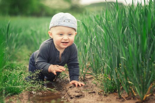 A Caucasian infant climbs in a muddy puddle and splashes into the water.