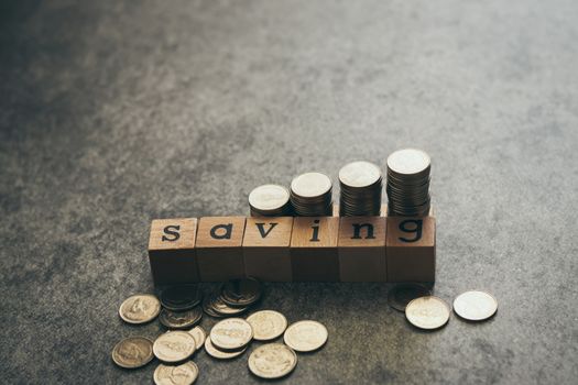 SAVING wood cube block with coin on black background with copy space. Concept of saving and deposit, business wealth, income or salary, debt and loan. Money save or invest for retrirement.