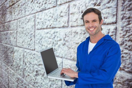 Handsome mechanic using laptop over white background against grey brick wall