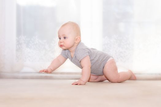 Caucasian infant walks on four on bright ground with very light background. Side view.