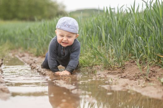 A Caucasian infant is playing in a muddy pool. Children's fun outdoors.