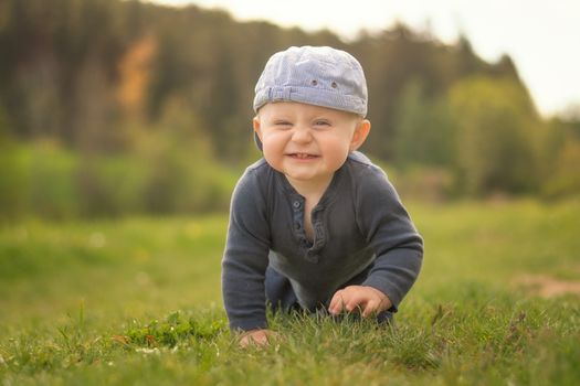 A Caucasian infant crawling on a meadow road. The boy laughs at the camera.