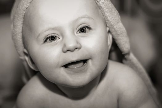 Black and white portrait of caucasian smiling baby in hooded bath towel looking upwards. Close up.