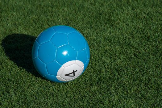 Blue number 4 soccer billiards or pool ball on green grass with a shadow and copy space. Concept of sports, recreation and childhood fun.