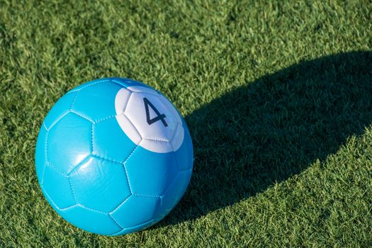 Blue number 4 soccer billiards or pool ball on green grass with a shadow and copy space. Concept of sports, recreation and childhood fun.