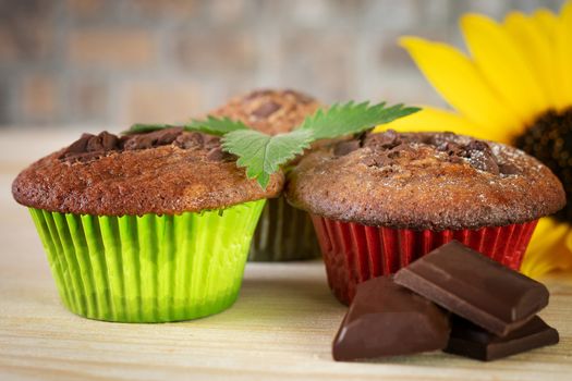 Muffins in colorful baskets with chocolate and sunflower on wooden table. Close up. Blurred foreground and background.