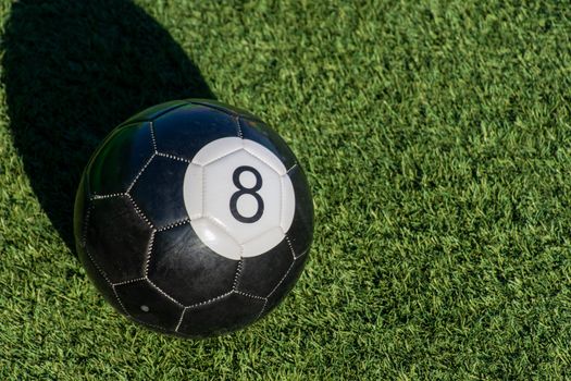 Black Eight (8) ball a soccer billiards or pool ball on green grass with a shadow and copy space. Concept of sports, recreation and childhood fun.