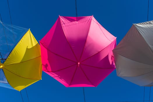 Colorful vibrant umbrellas hanging over the walking street for a festival on a blue sky sunny day close up of the pink umbrella.