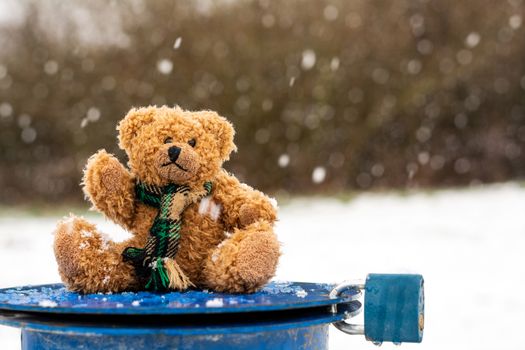 Plush teddy bear on blue lid with blue lock in snowy landscape with blurred background.