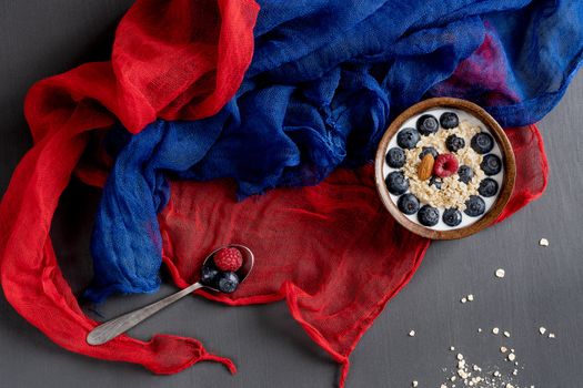 Healthy food. Bowl of oatmeal with blueberries, spoon, blue and red scarf on a gray table.