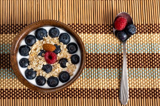 The concept of health. Yoghurt bowl with oat flakes, blueberries, raspberries and almond on a wooden tablecloth with a spoon.