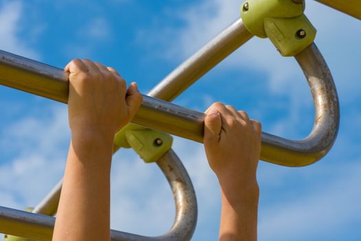 Two child's hand grabbing monkey bars at a playground conecept holding on strong preventing falling, swinging, and maintaining balance.