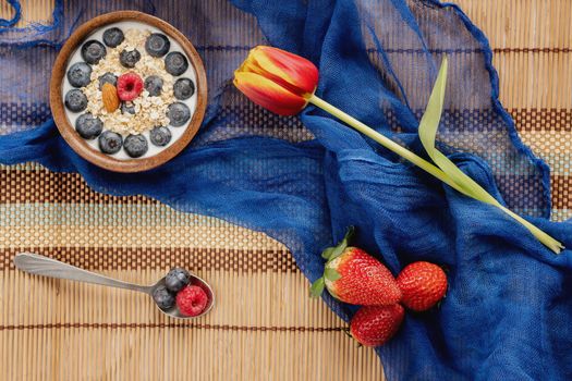 Valentine's Breakfast. Bowl of oatmeal with fruit on wooden tablecloth with tulip and blue scarf.