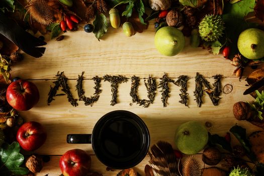 Autumn concept. A black cup of tea on a wooden table with a frame of autumn crops and falling leaves.