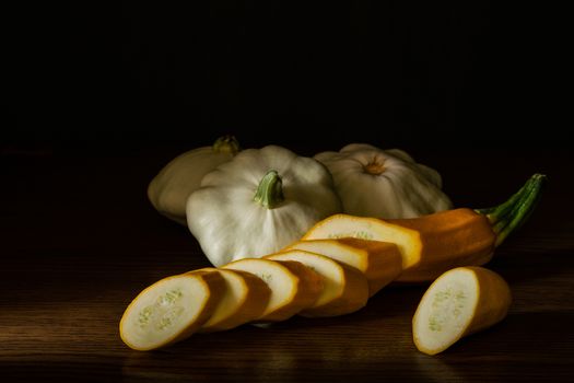 Chiaroscuro. Sliced ​​zucchini and three pastinas on a wooden table with black background.