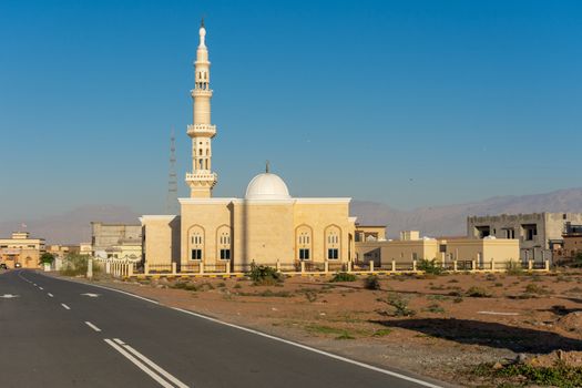 White Mosque in a residential area in the Middle East with a blue sky in the late afternoon sunshine looking towards the mountains.