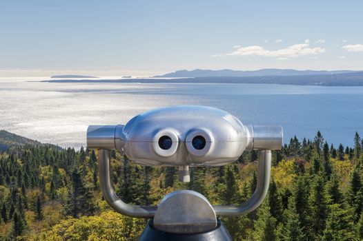 Public binoculars in front of a view over the Forillon National Park, Gaspe Peninsula, Quebec, Canada (montage)