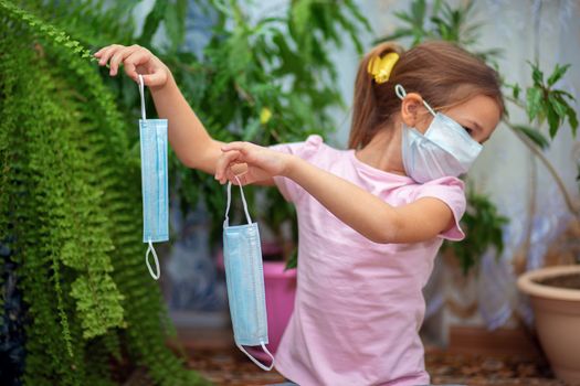 A little girl in a medical mask holds two more masks in her hands. Maximum protection during quarantine