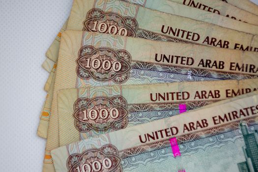 The Currency of the United Arab Emirates (UAE) - Thousand Dirham notes spread out on a white background. Money exchange.