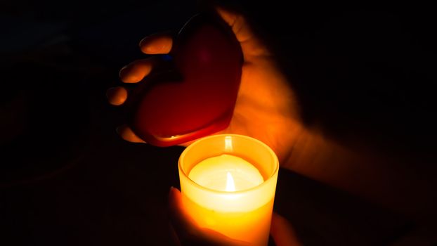 A fortune teller holds a heart in her hands and guesses at future love with a lighted candle. Christmas fortune telling and divinations. Red heart in the hands of a girl with a burning candle.