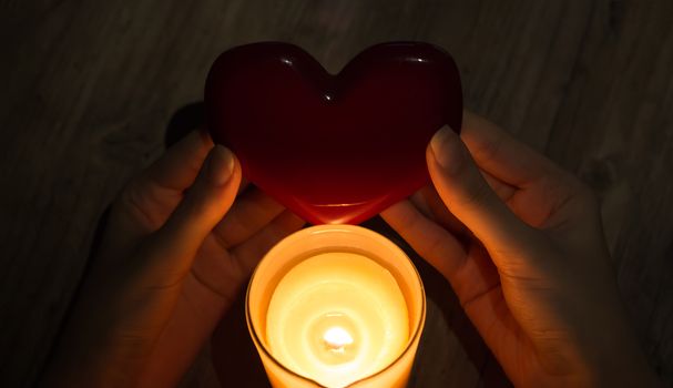 A fortune teller holds a heart in her hands and guesses at future love with a lighted candle. Christmas fortune telling and divinations. Red heart in the hands of a girl with a burning candle.