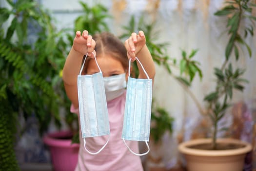 A little girl in a medical mask holds two more masks in her hands. Maximum protection during quarantine.