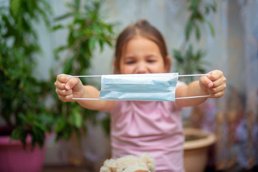 Little girl holds a medical mask in outstretched hands. The child puts on a protective mask