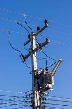 Electric pole connect to the high voltage electric wires on against bright blue sky.