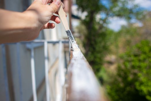 The process of painting rusty peeling rods on the fence. Man paints a brush with a fence, hand closeup. Spring work or repair