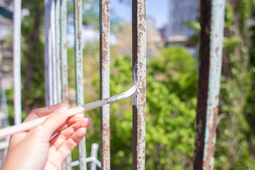 The process of painting rusty peeling rods on the fence. Man paints a brush with a fence, hand closeup. Spring work or repair