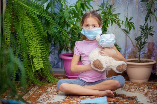 The girl put on a medical mask on herself and on her toy - a teddy bear. Quarantine and self-isolation during the epidemic of the virus