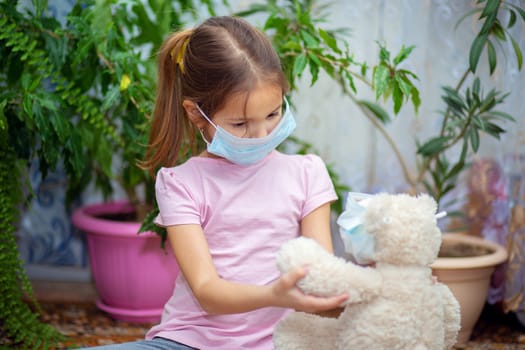 The girl put on a medical mask on herself and on her toy - a teddy bear. Quarantine and self-isolation during the epidemic of the virus