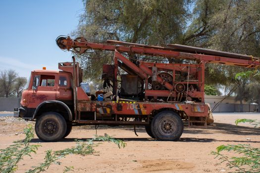 "RAK, RAK/UAE - 6/1/2019: A large red old antique broken down water machine truck parked in the sand by trees in the United Arab Emirates."