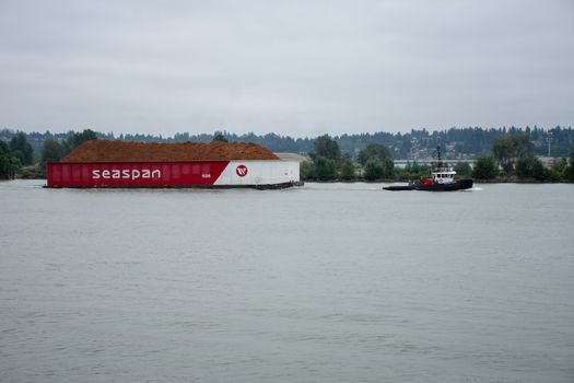 "New Westminster, BC/Canada - 8/2/2018: A Tugboat pulling a Seaspan barge in New Westminster, British Columbia, Canada looking from the Quay in the Fraser River near Surrey."