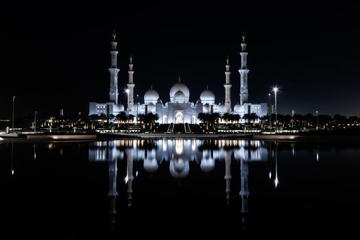 Iconic Islamic Site: Grand Mosque in Abu Dhabi, United Arab Emirates at night with a reflection in the pool showing off its beautiful colours of purple in the sky and water.