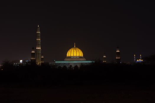 A Wide view of the Sultan Qaboos Grand Mosque and Al Ameen Mosque in Muscat, Oman at night showing off and glowing dome colours.