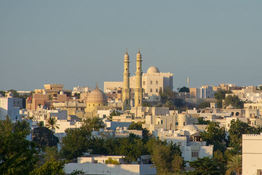 Common looking Middle Eastern city view at sunset. Muscat, Oman on the Arab Peninsula with mosques, residential houses and trees.