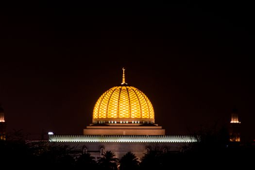 Glowing center dome of an Islamic mosque Sultan Qaboos Grand Mosque with a night blue sky in the Middle East.