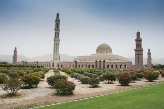 Sultan Qaboos Grand Mosque, Muscat, Oman during the afternoon in the blue sky and clouds and mountains in view.